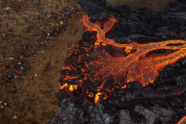 Aerial view of lava flowing from the Geldingadalur crater and the audience gathered to admire it