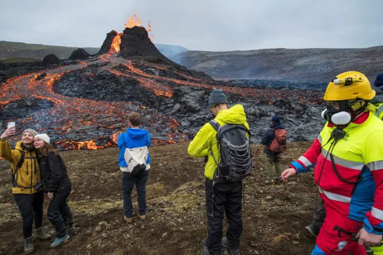 Tourists catch a selfie with the flowing lava in Geldingadalur on the Reykjanes peninsula while a search-and-rescue volunteer monitors the area
