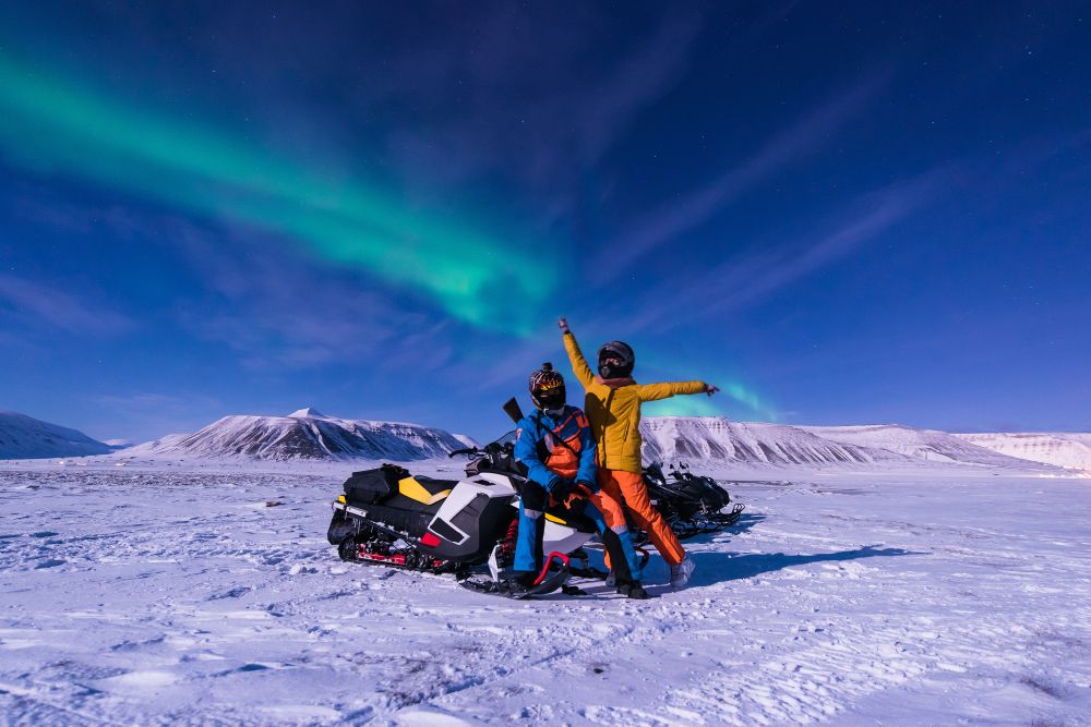 Snowmobilers in Iceland pose in front of the Northern Lights
